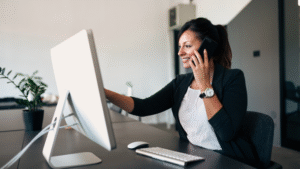 A woman talking on the phone while pointing at a computer screen.