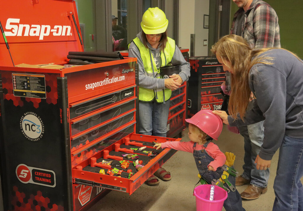 A child reaches for candy from a Snap-on toolbox at the Career and Corporate Training display during the Community Trick-or-Treat event. The table, led by Dr. Joni M. Gray, featured toolboxes filled with treats for families.