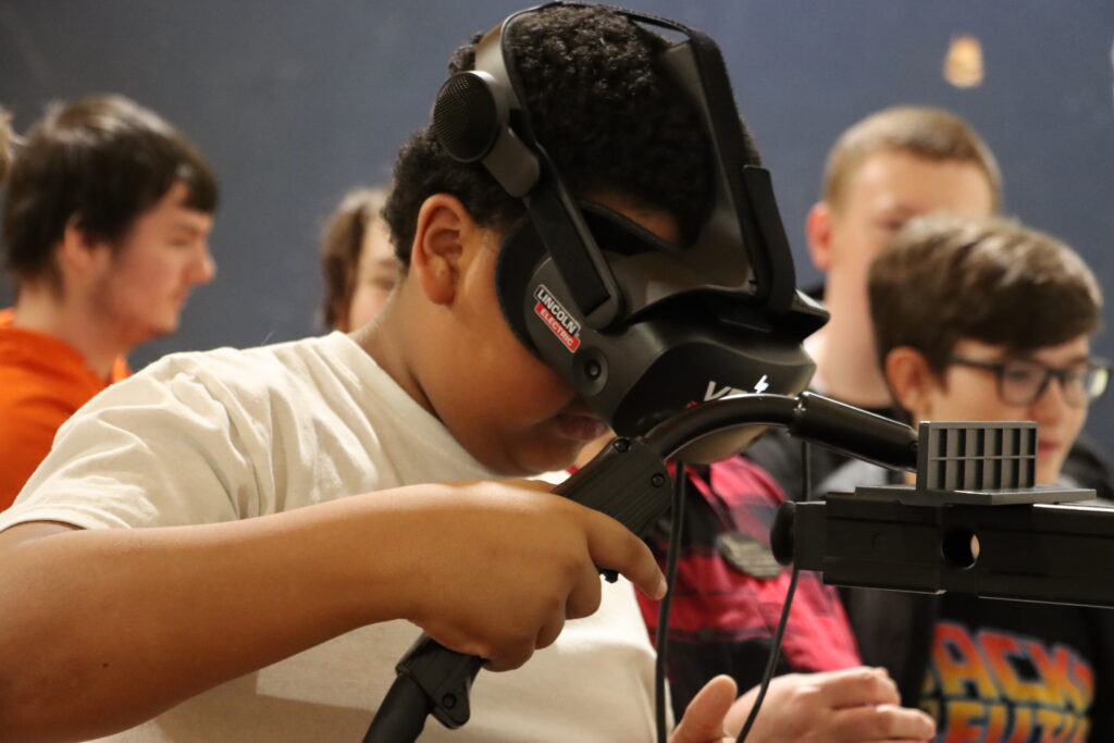 A photo of a student testing their technical skills with a hands-on VR welding simulator.