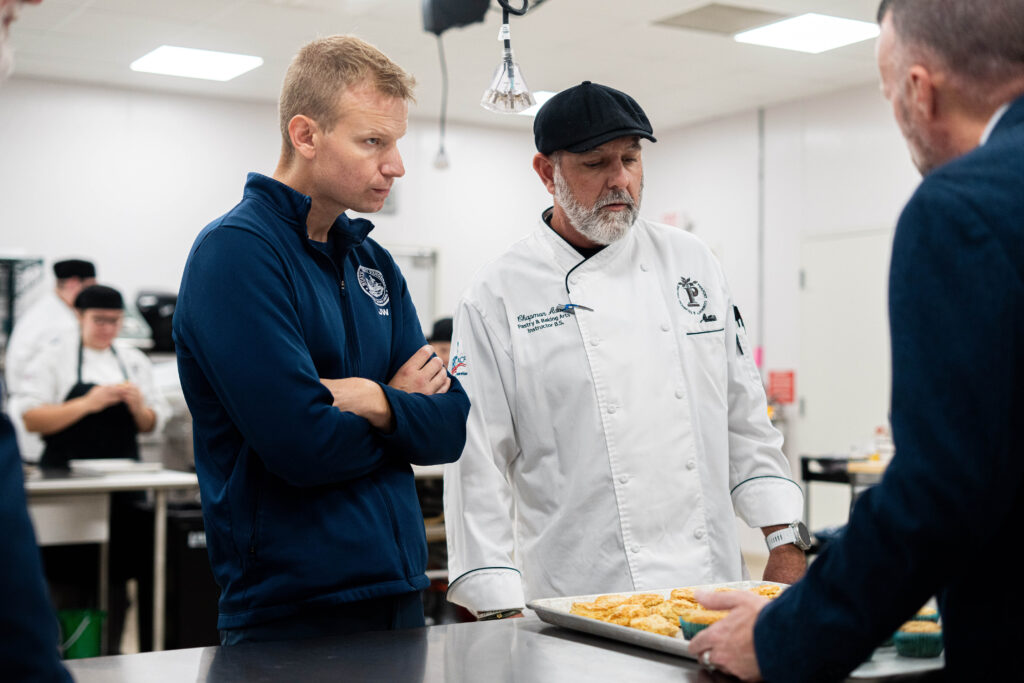 Pierpont Photo. Delegate John Williams, left, learns about student pastry and baking projects from Chapman “Chappy” Adair, instructor of Pastry and Baking, during a visit to Pierpont Community & Technical College’s Culinary Academy on Tuesday.