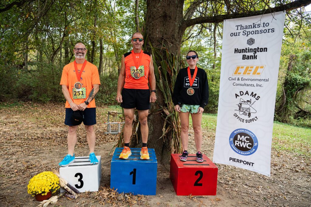 The top three overall finishers of the inaugural Fall in Love with Health 5K pose on the awards podium following the race at Prickett’s Fort State Park in Fairmont, W.Va. From left are third-place finisher Christopher Hedio, first-place finisher Brian Narog and second-place finisher Stefanie Moore.