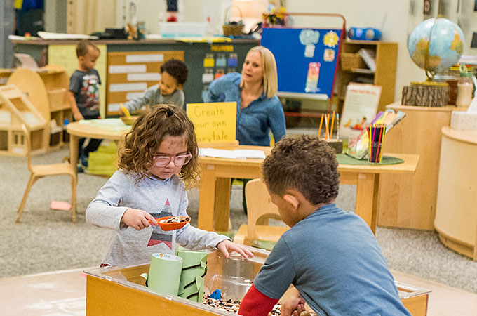 Teacher and young students playing in a classroom table top sandbox