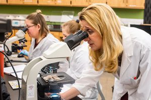 Three woman in white lab coats looking under microscopes