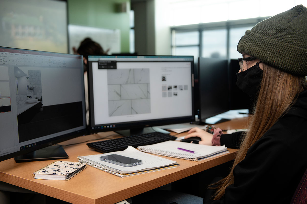 Woman wearing knit hat and face mask looking at images of tile on a computer
