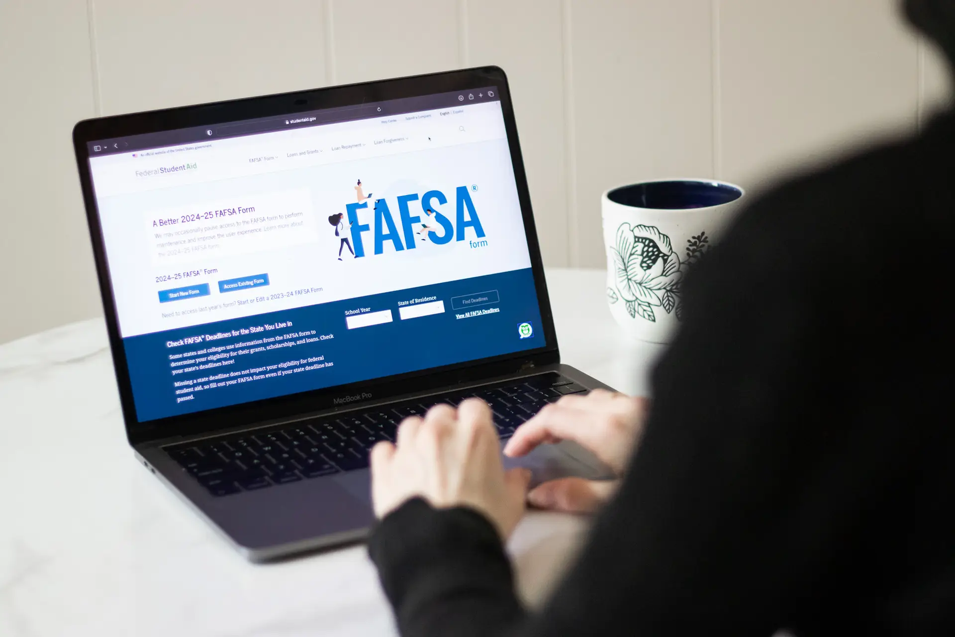 A person is displayed in front of a computer screen with the Better FAFSA page on the screen.