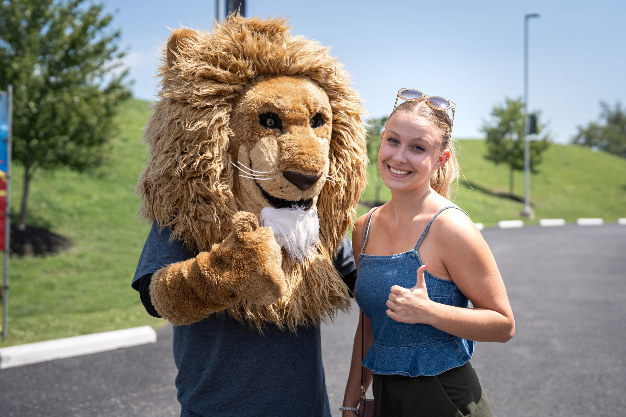 A student is pictured giving a thumbs up with a lion mascot character.