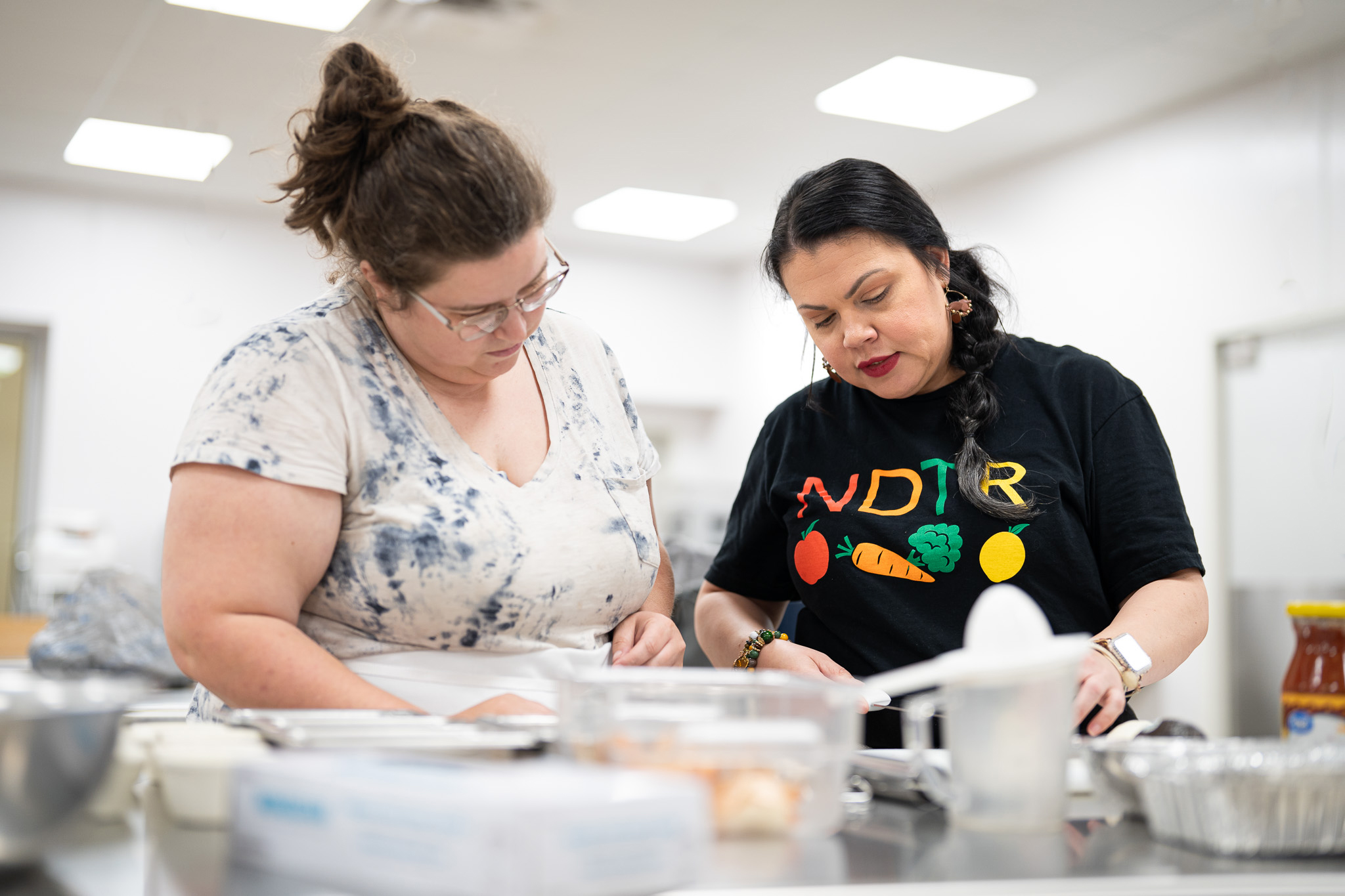 Two female individuals are featured in a kitchen setting while preparing a meal.