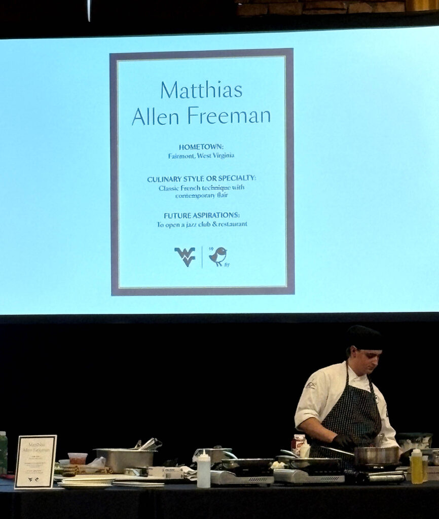Freeman works his station beneath an introduction slide as judges evaluate dishes during the 3rd Annual WVU Culinary Competition at Nemacolin.