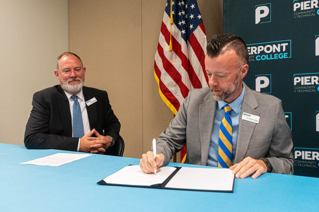 Dr. Michael Waide, President of Pierpont Community & Technical College, signs a memorandum of agreement creating a new educational pathway for eligible Pierpont employees. Looking on is David Beighley, Provost and Vice President of Academic Affairs at Pierpont.