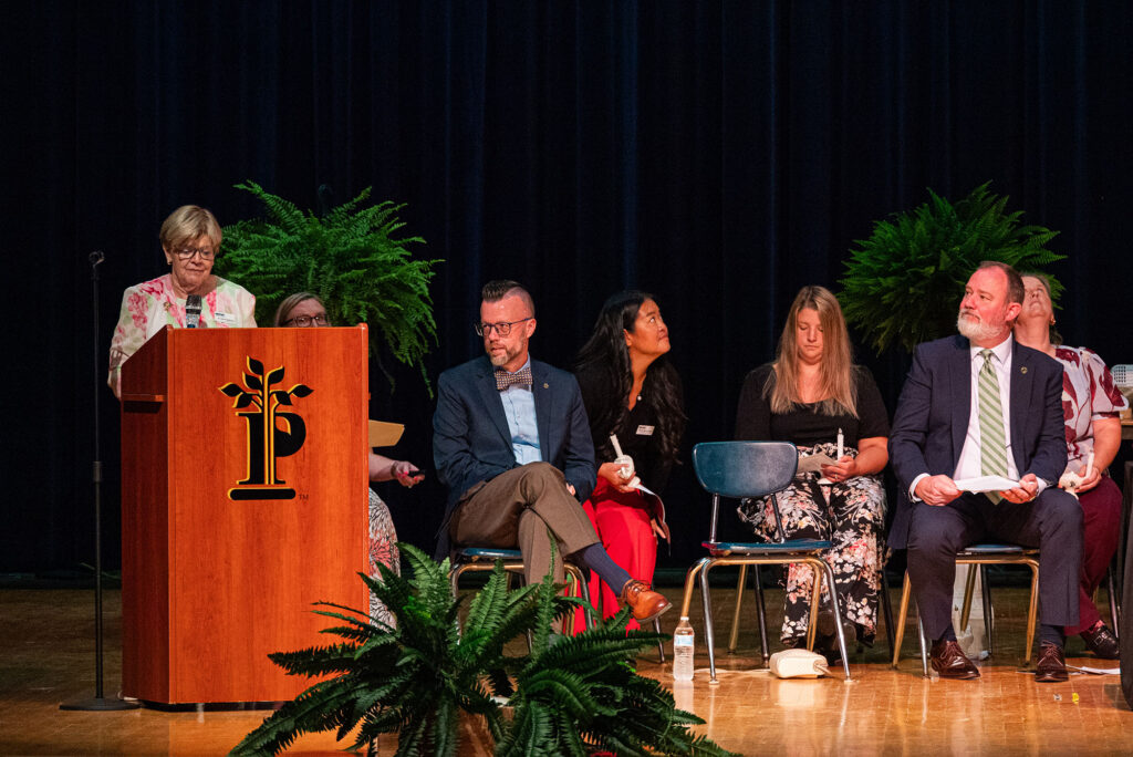 Dr. Joanne Seasholtz, a member of the Pierpont Community & Technical College Board of Governors, speaks from the podium during the Licensed Practical Nursing Pinning Ceremony as graduates and college leaders participate in the ceremony on stage.