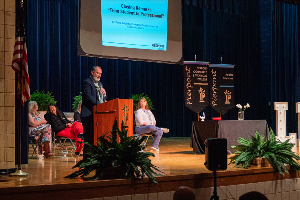 David Beighley, provost and vice president of academic affairs, delivers closing remarks during Pierpont Community & Technical College's Licensed Practical Nursing Pinning Ceremony. Faculty members are seated on stage as Beighley addresses graduates and guests.